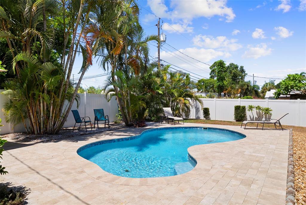 A kidney-shaped swimming pool sits on a paved patio surrounded by palm trees and fencing — 14480 120TH AVENUE, LARGO, FL