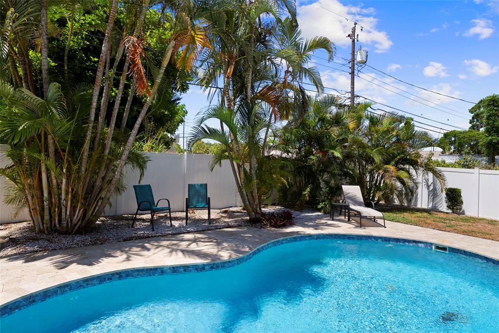 A swimming pool with a patio, lounge chairs, and palm trees against a white fence — 14480 120TH AVENUE, LARGO, FL