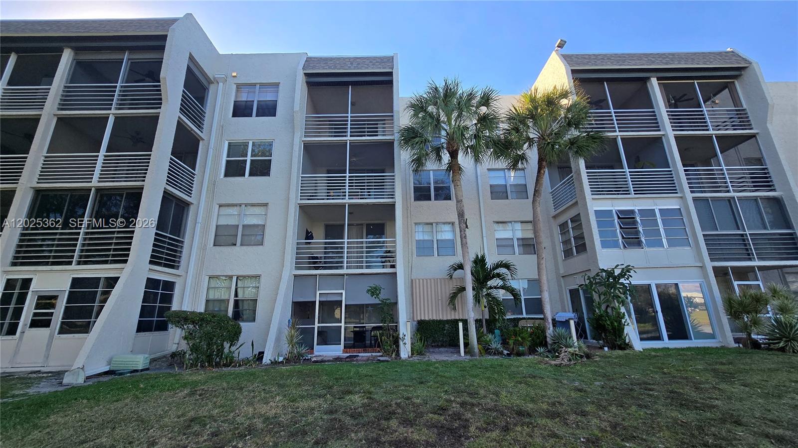 A multi-story apartment building features screened balconies and palm trees on a grassy lawn — 9230 Lagoon Pl # 310, Davie FL 33324, DAVIE, FL