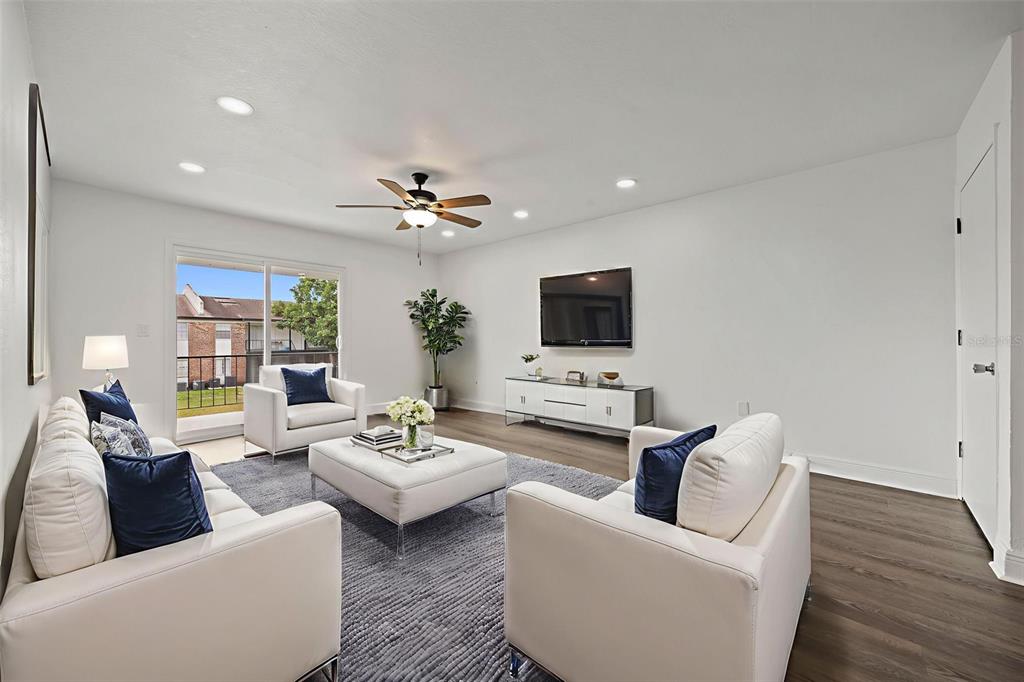 A living room features white furniture, a gray area rug, a television, and a sliding door — 5317 CURRY FORD ROAD 203 - BLDG L, ORLANDO, FL