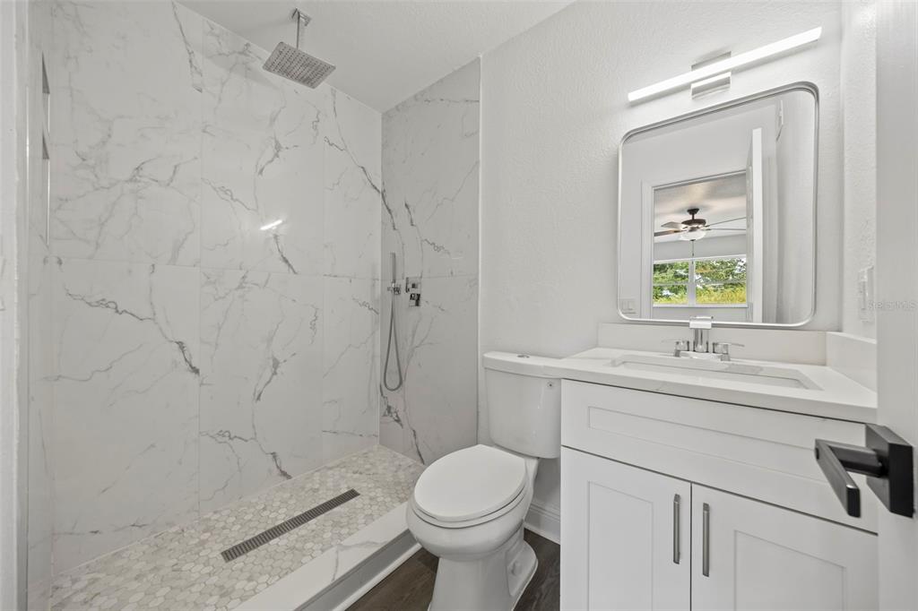 A modern bathroom features a walk-in marble tile shower, a white vanity, and a toilet — 5317 CURRY FORD ROAD 203 - BLDG L, ORLANDO, FL