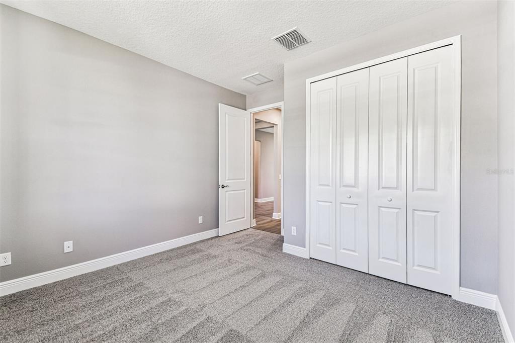 An empty bedroom features gray walls, gray carpeting, a white closet, and an open doorway — 1664 DRUMMOND POINT, ZEPHYRHILLS, FL
