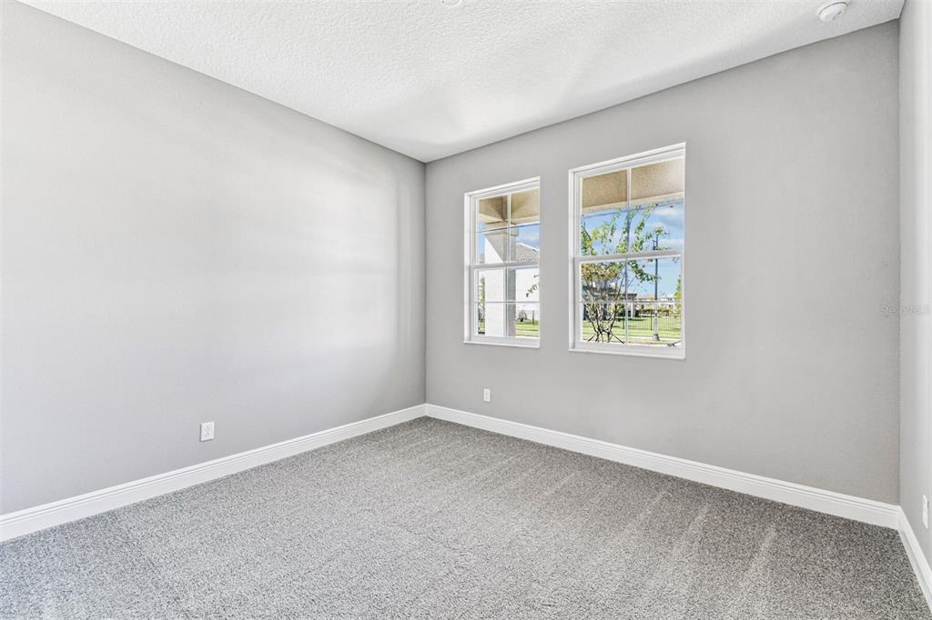 An empty room with gray walls, gray carpet, and two windows overlooking a neighborhood — 1664 DRUMMOND POINT, ZEPHYRHILLS, FL
