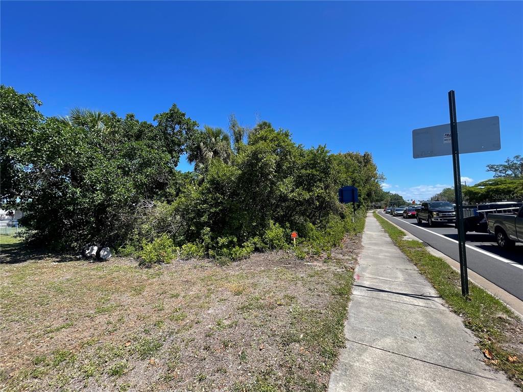 A sidewalk runs alongside a dense patch of trees and shrubs next to a road — 1519 MANATEE AVENUE E, BRADENTON, FL