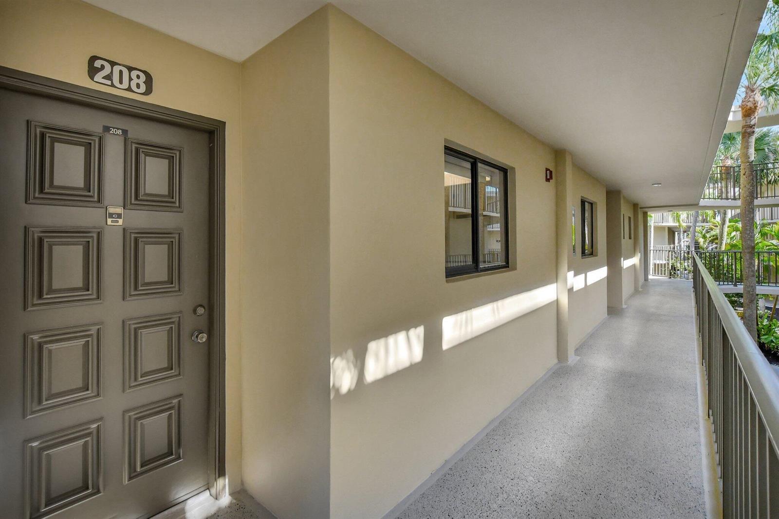An exterior hallway with a gray door labeled 208, beige walls, and a metal railing — 5340 Las Verdes Circle # 208, Delray Beach FL 33484, DELRAY BEACH, FL