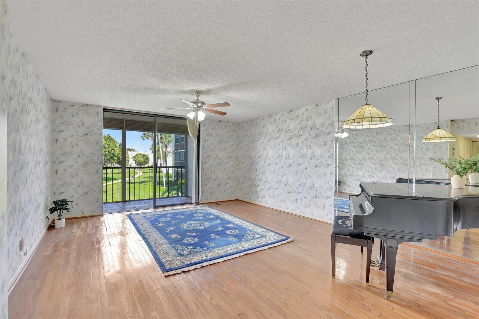 A living room with hardwood floors, floral wallpaper, a grand piano, and a sliding glass door — 5340 Las Verdes Circle # 208, Delray Beach FL 33484, DELRAY BEACH, FL