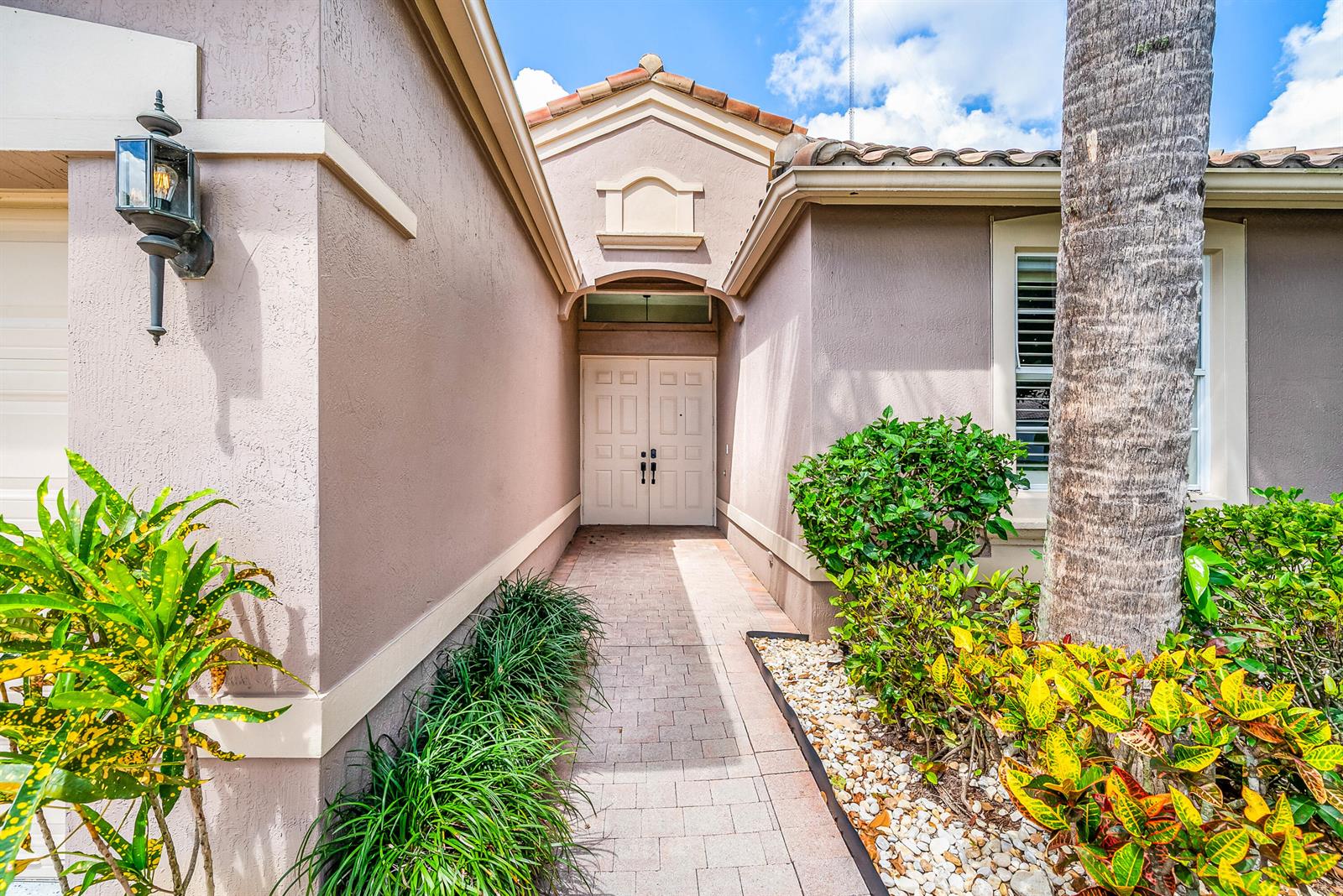 A paved walkway leads to the double front doors of a stucco house with landscaping — 9989 Torino Drive, Lake Worth FL 33467, LAKE WORTH, FL