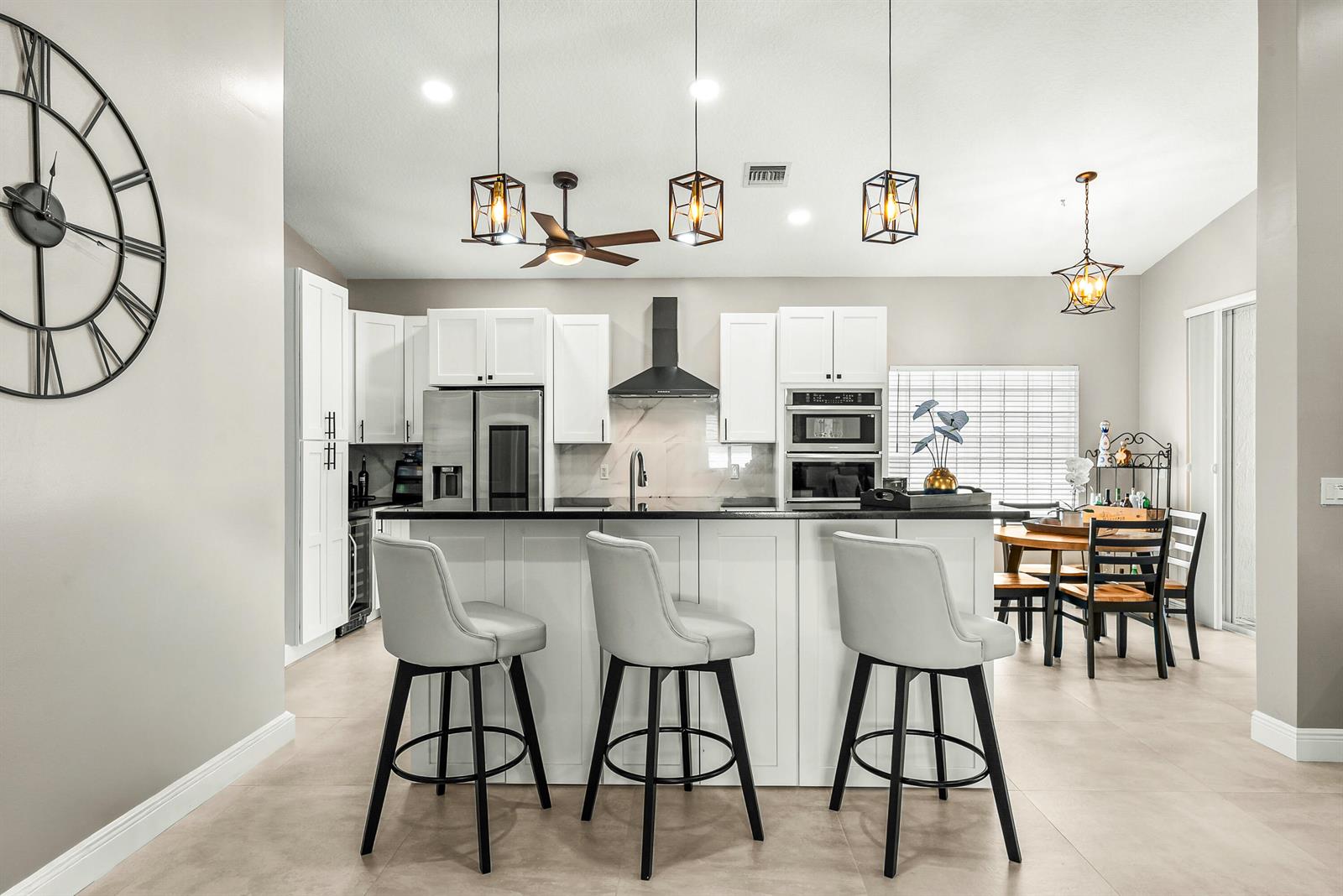 A modern kitchen features white cabinetry, a black island with bar stools, and pendant lighting — 9989 Torino Drive, Lake Worth FL 33467, LAKE WORTH, FL