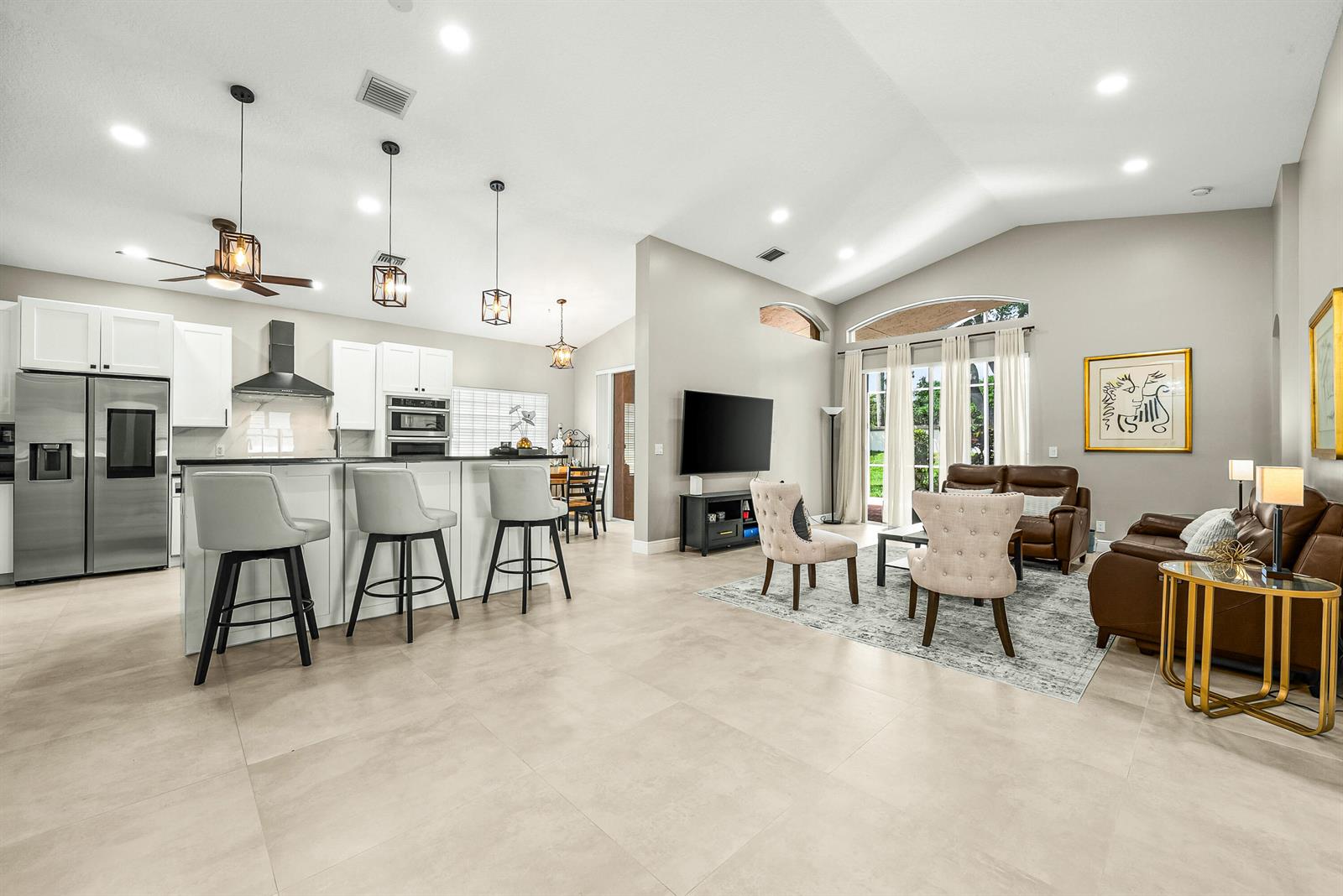 An open-concept kitchen and living room featuring light tile flooring, white cabinetry, and vaulted ceilings — 9989 Torino Drive, Lake Worth FL 33467, LAKE WORTH, FL