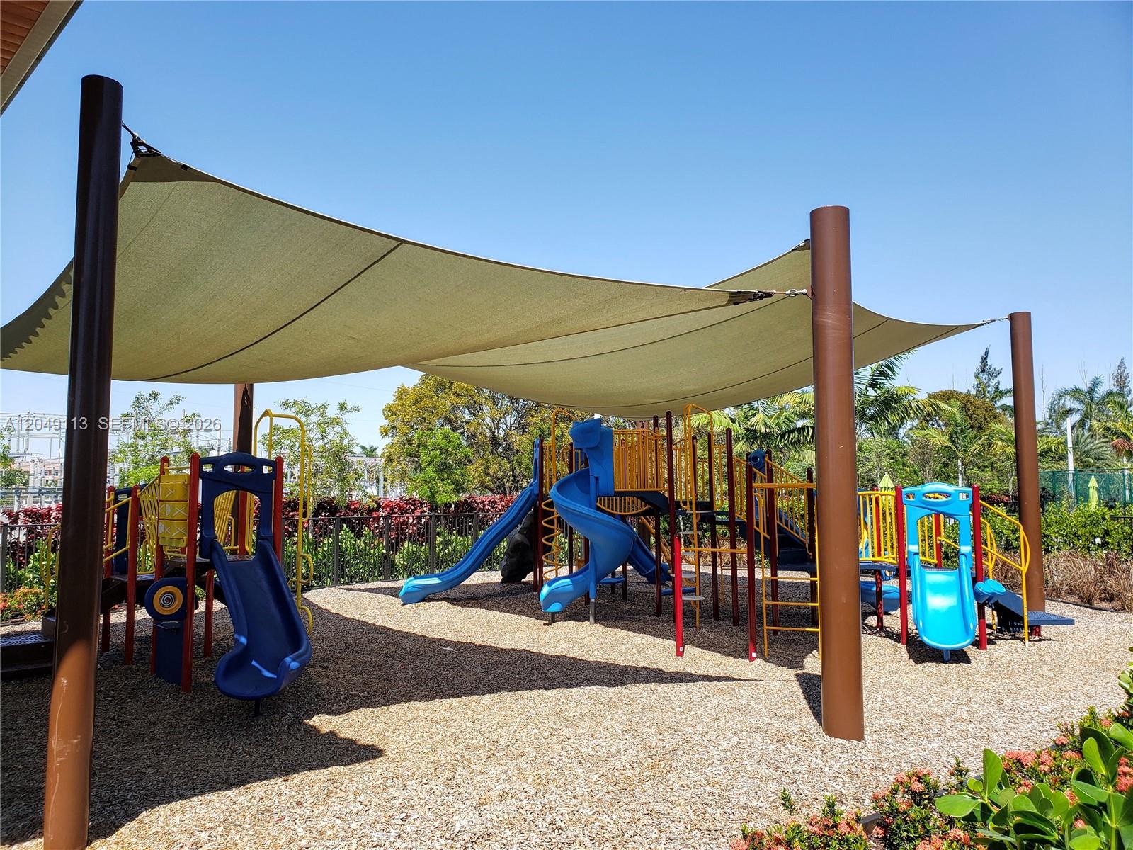 A playground features multiple blue slides and a large shade canopy over wood chips — 10620 NW 88th St # 223, Doral FL 33178, DORAL, FL