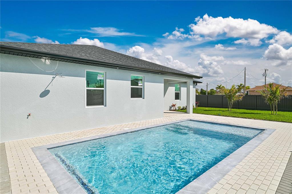 A backyard swimming pool sits on a paved patio beside a light-colored house exterior — 1326 NE 7TH PLACE, CAPE CORAL, FL