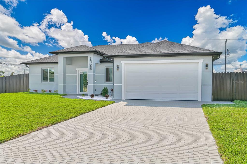 A single-story house with a light gray exterior, a white garage door, and a paved driveway — 1326 NE 7TH PLACE, CAPE CORAL, FL