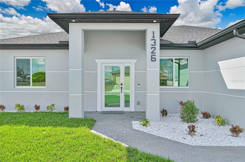 The exterior of a modern, light-gray house features a paved walkway leading to the front door — 1326 NE 7TH PLACE, CAPE CORAL, FL