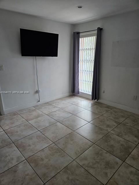 A room with light-colored tile flooring, a wall-mounted television, and a window with curtains — 9483 SW 76th St # N8, Miami FL 33173, MIAMI, FL