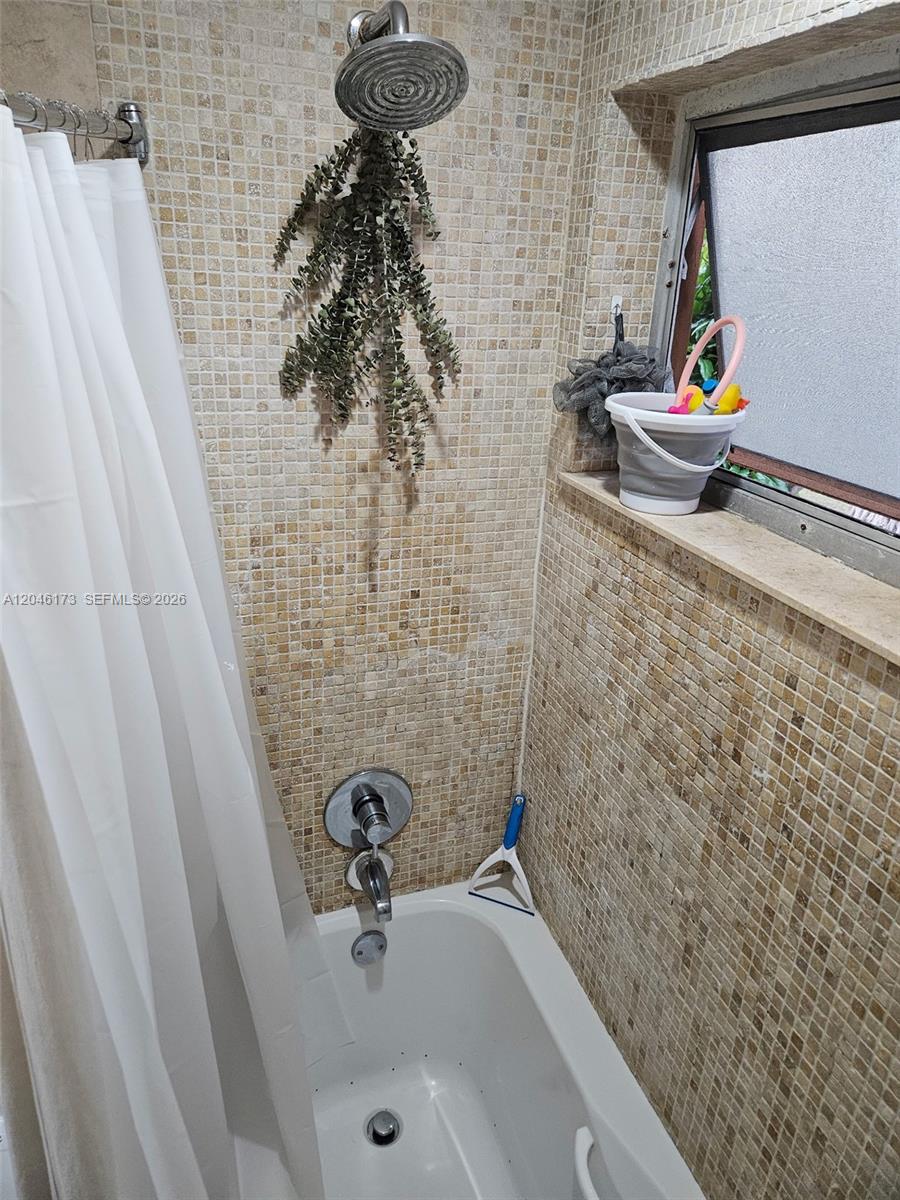A shower stall features a tiled wall, a showerhead with hanging greenery, and a window — 9483 SW 76th St # N8, Miami FL 33173, MIAMI, FL