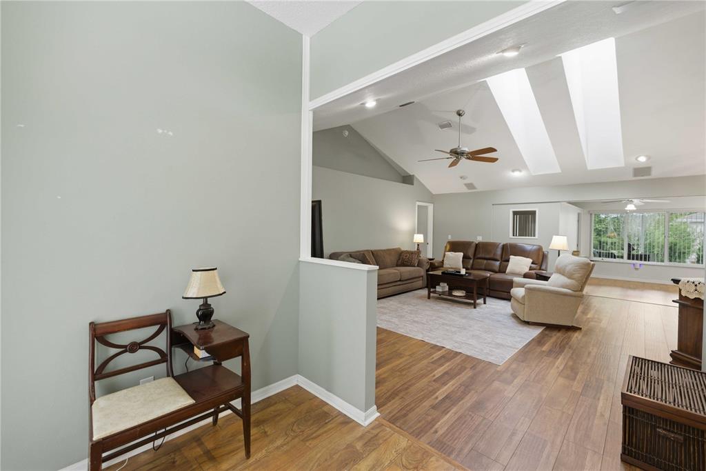 A living room with vaulted ceilings, skylights, and wood-look flooring viewed from an entryway — 8490 SW 60TH COURT, OCALA, FL