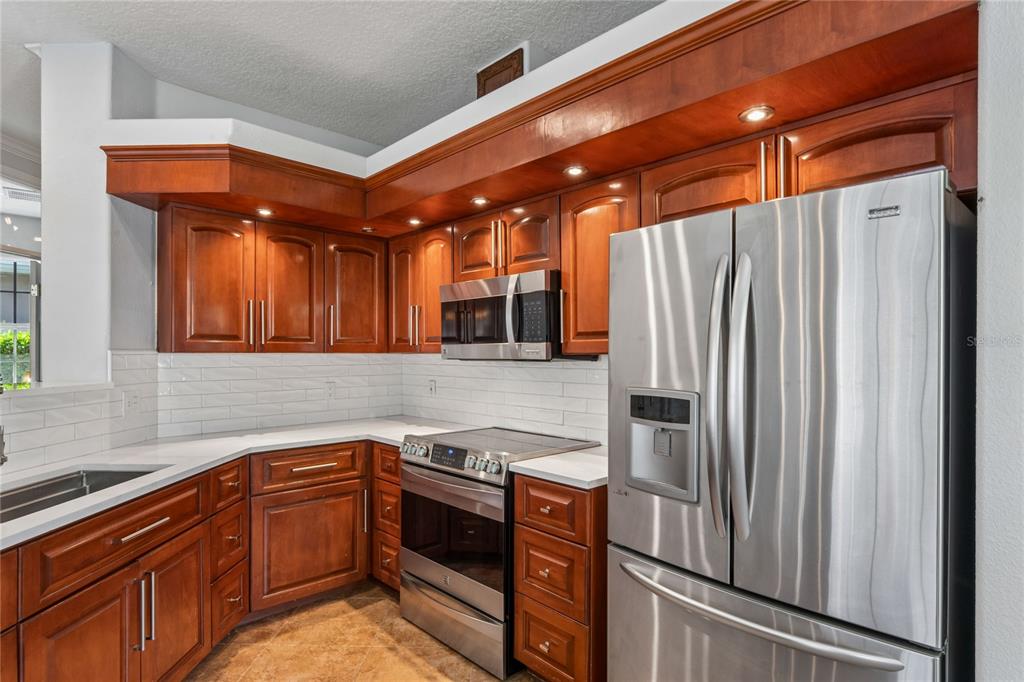 A kitchen features cherry wood cabinets, stainless steel appliances, white countertops, and a tile backsplash — 4354 BURNBERRY GLEN CT, SPRING HILL, FL
