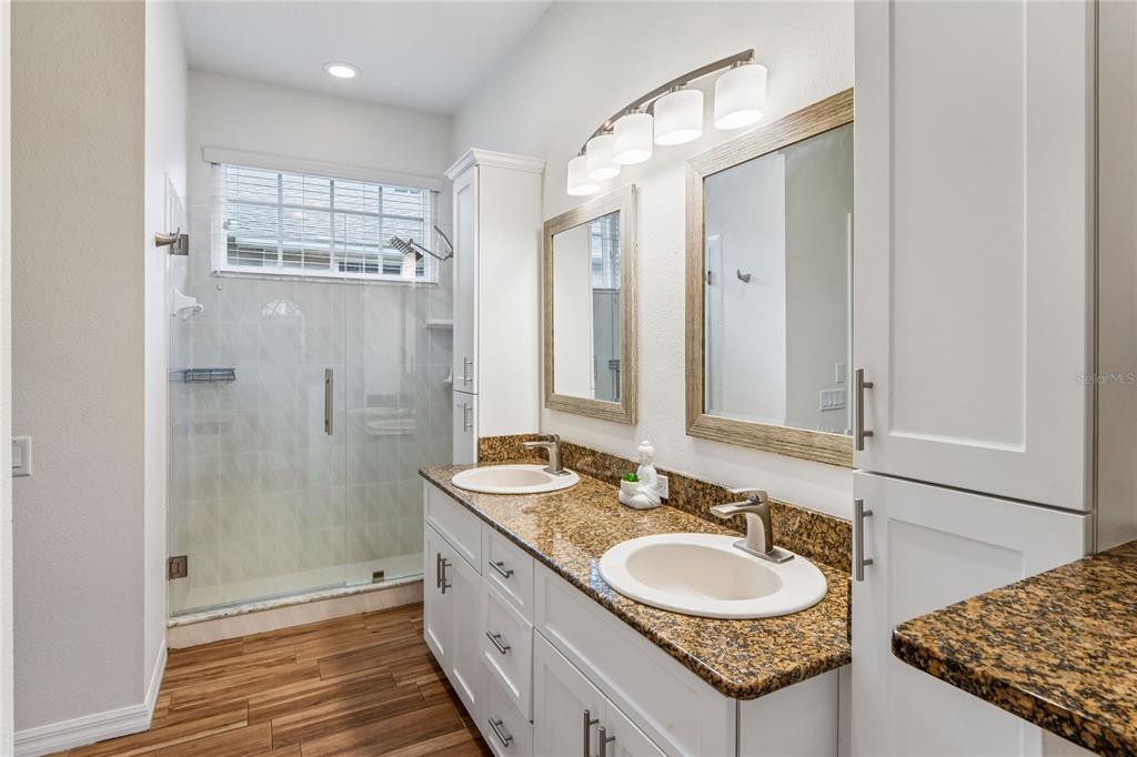 A bathroom features a double vanity with granite countertops, white cabinets, and a glass shower — 4354 BURNBERRY GLEN CT, SPRING HILL, FL