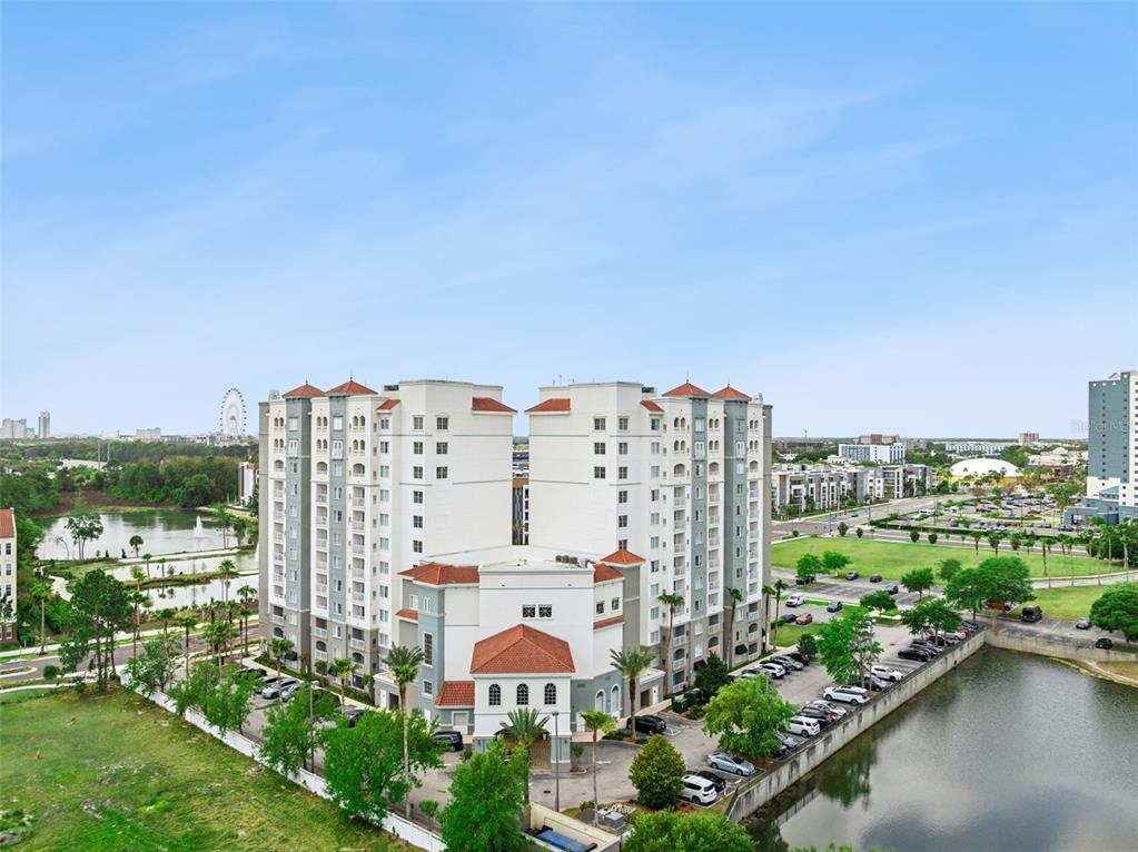 An aerial view shows a large multi-story apartment building with a parking lot and pond — 7395 UNIVERSAL BOULEVARD UNIT 1205, ORLANDO, FL