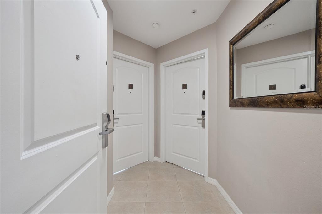 An entryway features light-colored tile flooring, three white doors, and a decorative wall mirror — 7395 UNIVERSAL BOULEVARD UNIT 1205, ORLANDO, FL