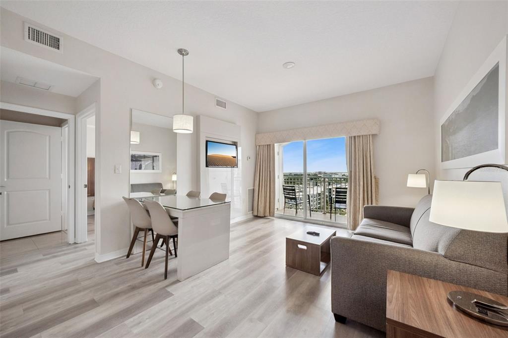 A living room features light wood floors, a dining area, and a balcony with views — 7395 UNIVERSAL BOULEVARD UNIT 1205, ORLANDO, FL