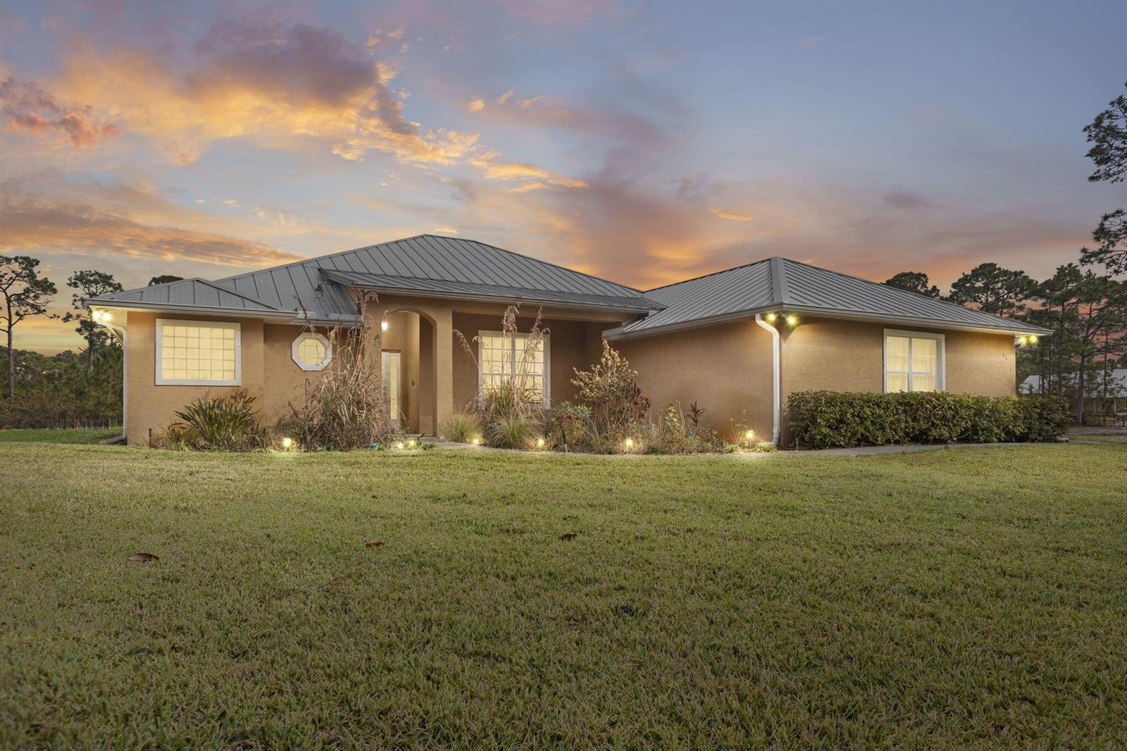 A single-story tan stucco house with a metal roof sits on a grassy lawn — 5224 Southwind Trail, Fort Pierce FL 34951, FORT PIERCE, FL