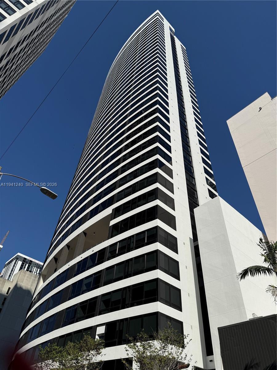 A low-angle view of a tall, modern white residential skyscraper against a clear blue sky — 225 N MIAMI AVE # 3505, Miami FL 33132, MIAMI, FL