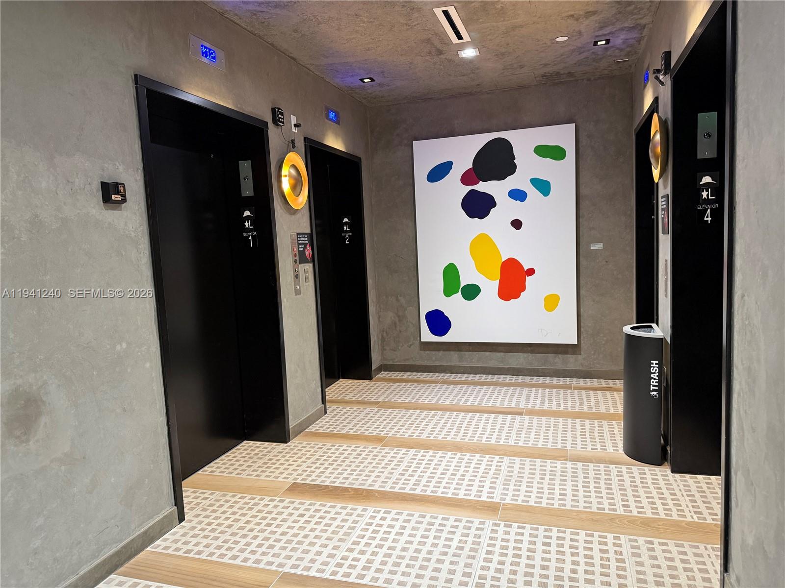 An elevator lobby features concrete walls, black elevator doors, a large abstract painting, and tiled flooring — 225 N MIAMI AVE # 3505, Miami FL 33132, MIAMI, FL