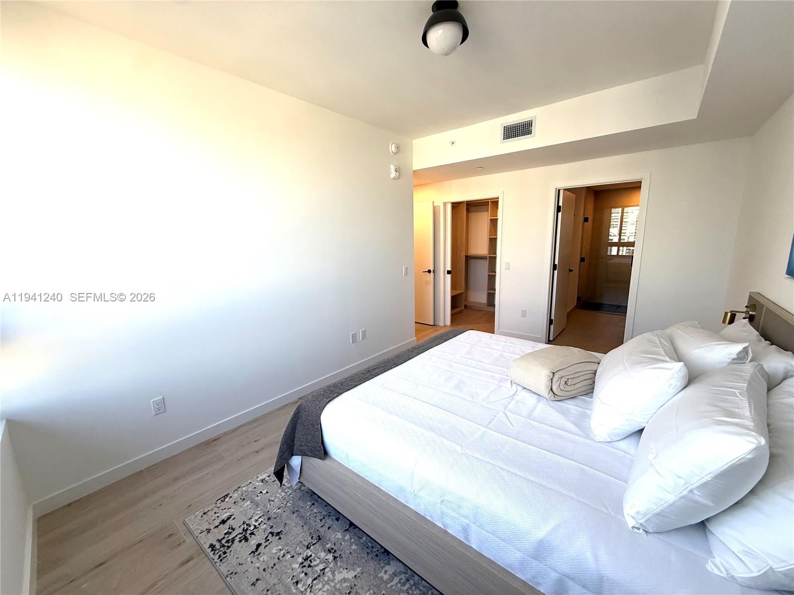 A bedroom features a bed, light wood flooring, a walk-in closet, and an attached bathroom — 225 N MIAMI AVE # 3505, Miami FL 33132, MIAMI, FL