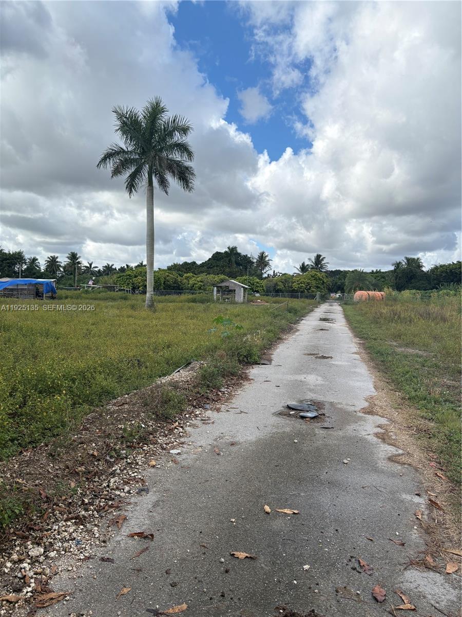 A narrow, weathered paved path leads through a grassy field toward trees and a small structure — Krome Avenue, Miami FL 33196, MIAMI, FL