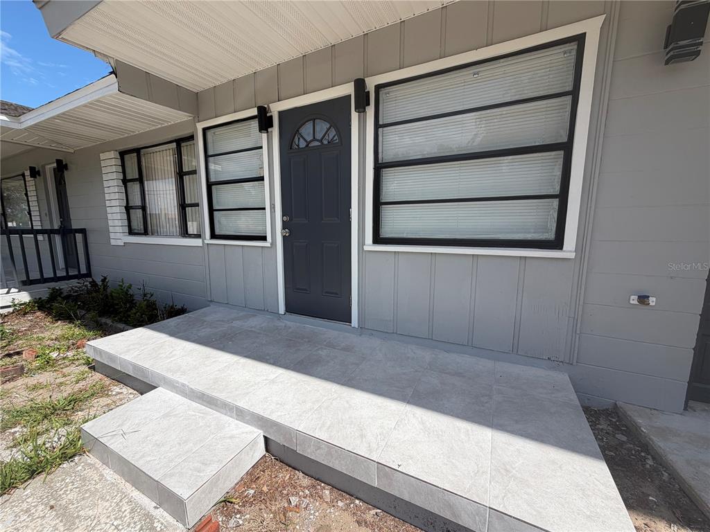 A gray house exterior features a tiled front porch, a dark door, and black-framed windows — 131 W ATWATER AVENUE, EUSTIS, FL