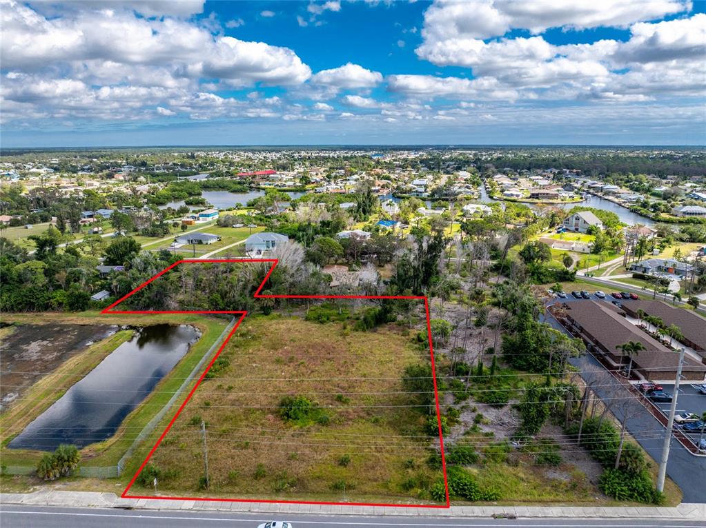 An aerial view shows a vacant, rectangular lot outlined in red next to a pond — 1701 PLACIDA ROAD, ENGLEWOOD, FL