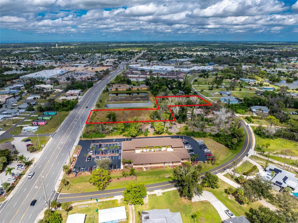 An aerial view shows a vacant, rectangular lot outlined in red next to a commercial building — 1701 PLACIDA ROAD, ENGLEWOOD, FL