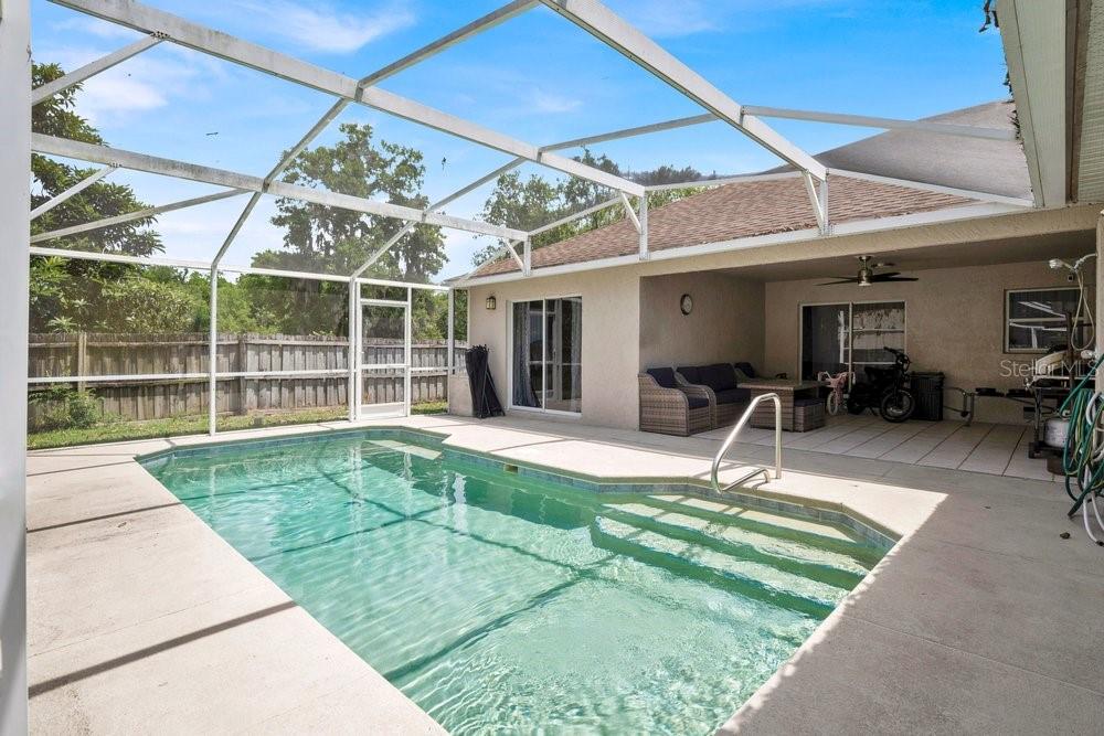 A swimming pool with a screened enclosure sits on a patio next to a house — 213 BRUSHCREEK DRIVE, SANFORD, FL