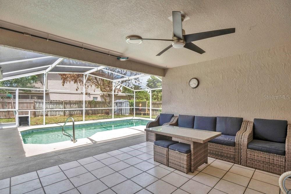 A covered patio features a wicker sofa set, a ceiling fan, and a screened-in pool — 213 BRUSHCREEK DRIVE, SANFORD, FL