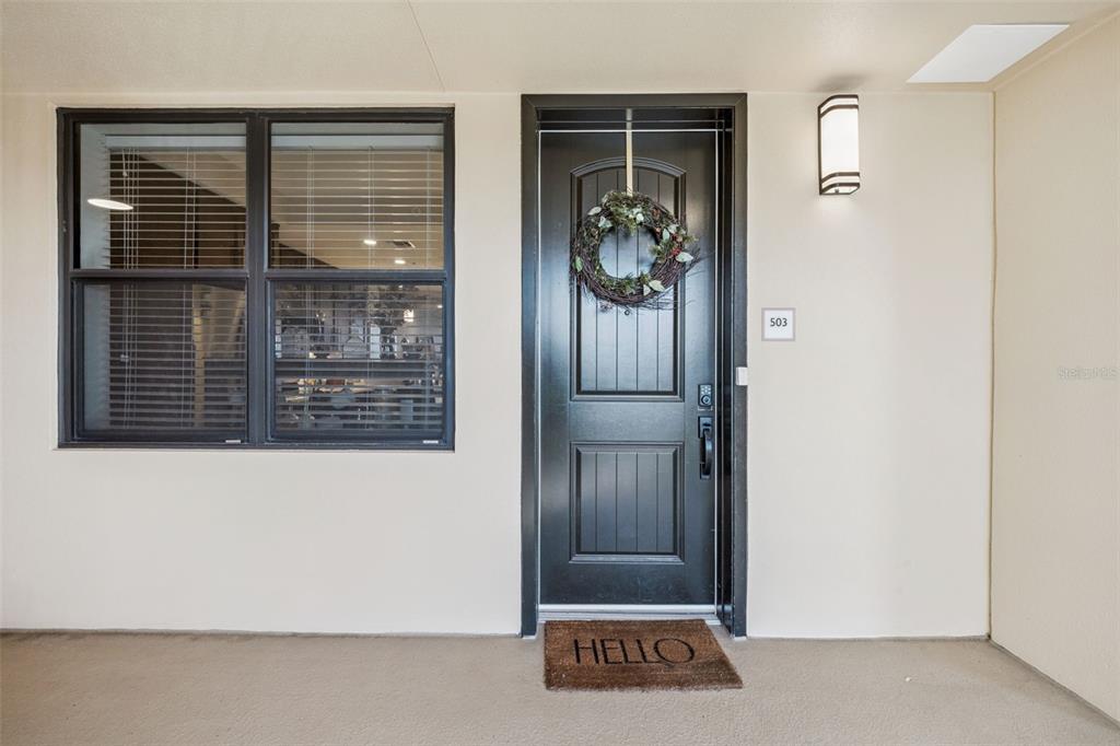 A black front door with a wreath and a welcome mat sits beside a window — 16300 COUNTY ROAD 455 UNIT 503, MONTVERDE, FL
