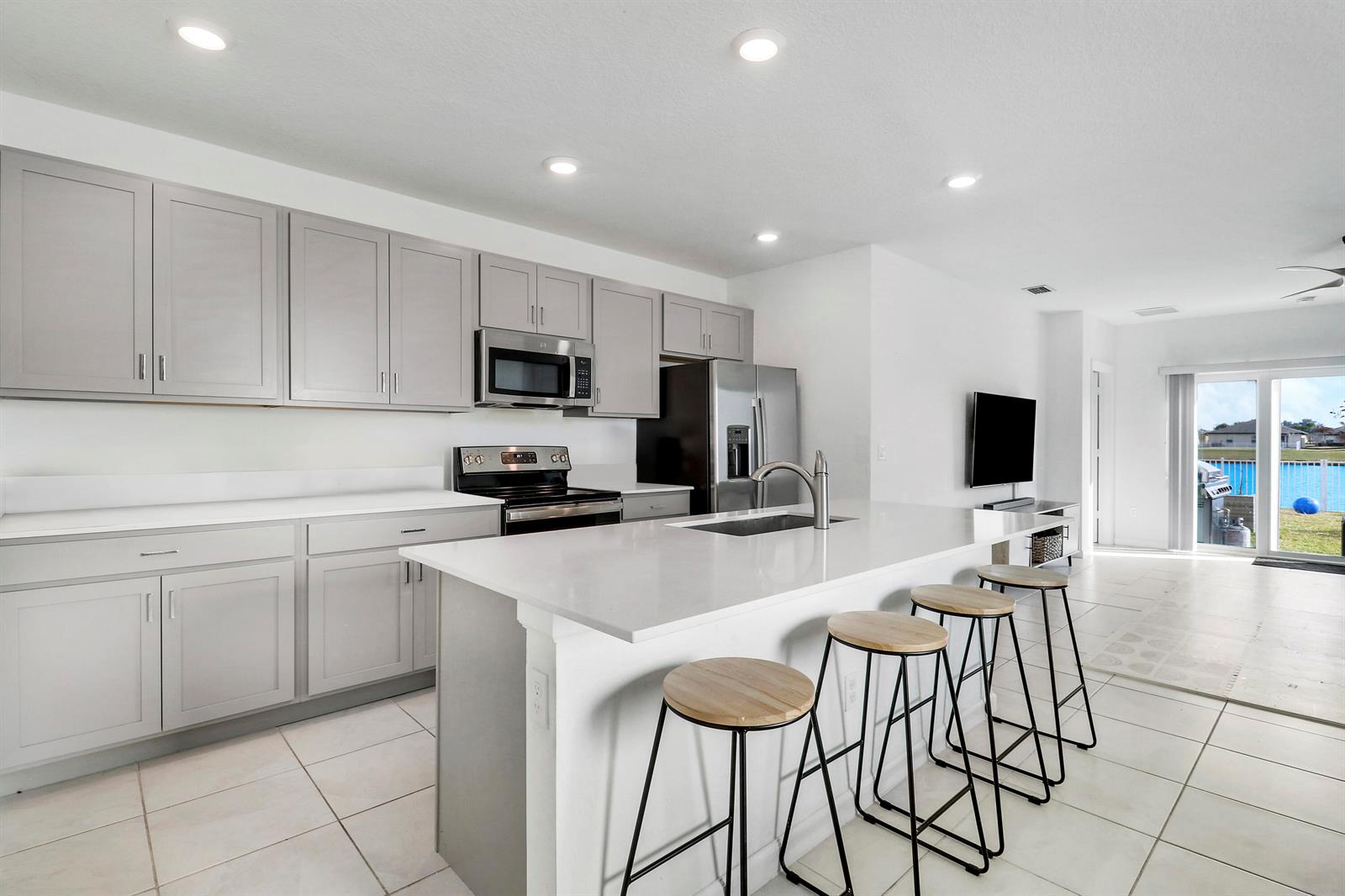 A modern kitchen features gray cabinets, white countertops, a central island, and bar stools — 4233 Troon Place, Fort Pierce FL 34947, FORT PIERCE, FL