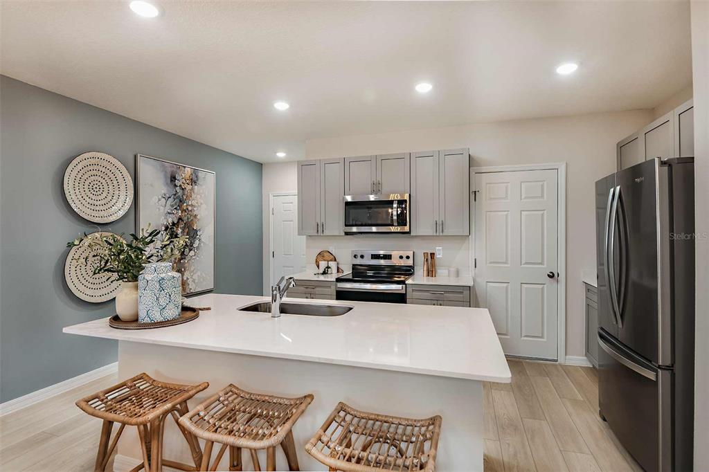 A kitchen features a white island, gray cabinets, stainless steel appliances, and light wood flooring — 4254 HILLOCK BOULEVARD, HAINES CITY, FL