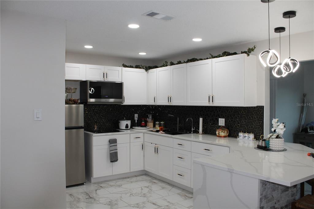 A kitchen features white cabinets, a black geometric backsplash, stainless steel appliances, and quartz countertops — 7423 STAR DUST DRIVE, PORT RICHEY, FL