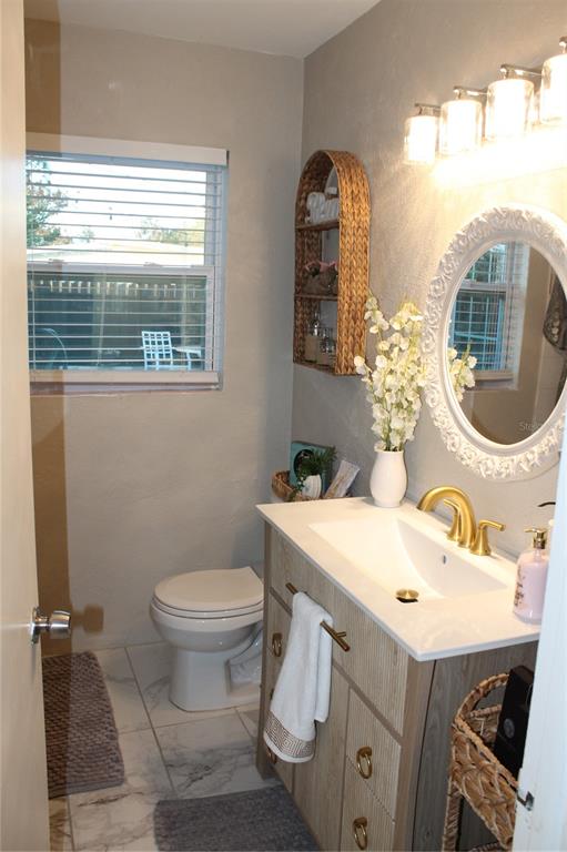 A bathroom features a vanity with a gold faucet, a round mirror, and a toilet — 7423 STAR DUST DRIVE, PORT RICHEY, FL