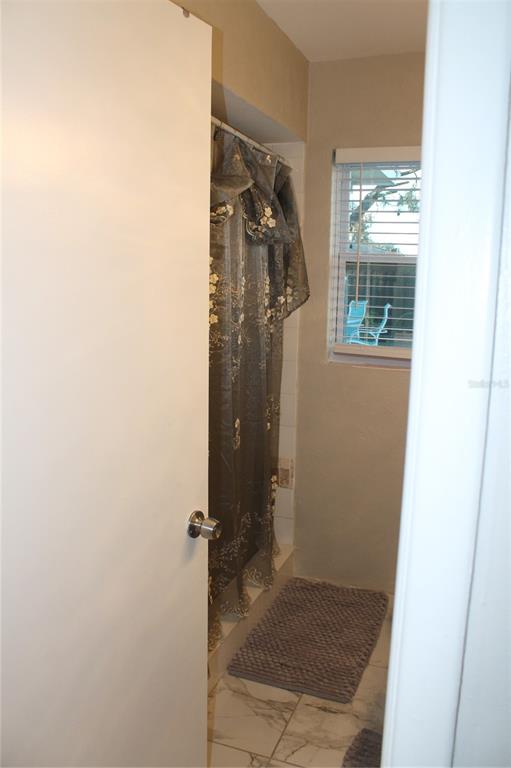 A bathroom features a shower with a decorative curtain, marble-look tile flooring, and a window — 7423 STAR DUST DRIVE, PORT RICHEY, FL