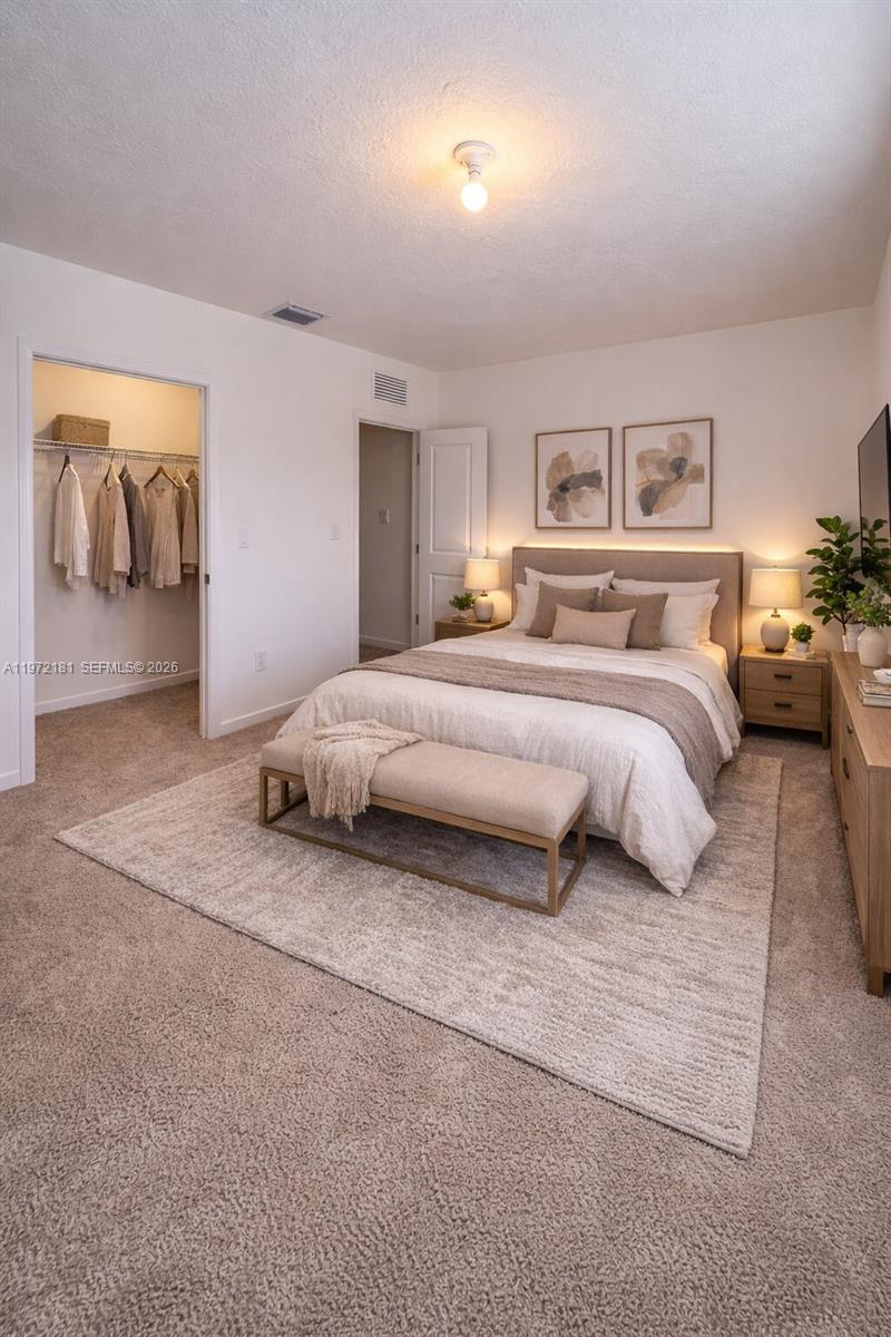 A bedroom features a bed with neutral bedding, a bench, a rug, and an open closet — 1765 SE 7th Ter, Homestead FL 33034, HOMESTEAD, FL