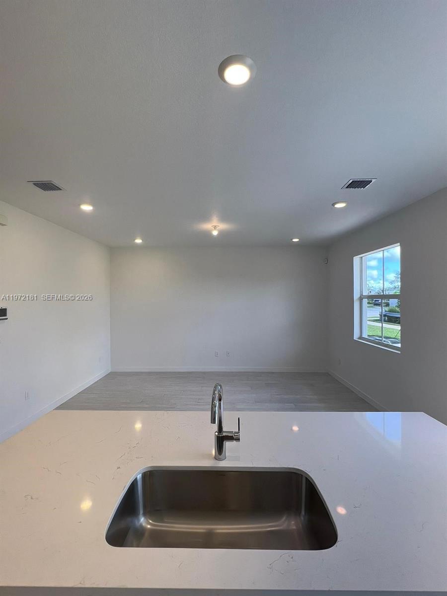 A kitchen island with a stainless steel sink overlooks an empty room with recessed lighting — 1765 SE 7th Ter, Homestead FL 33034, HOMESTEAD, FL