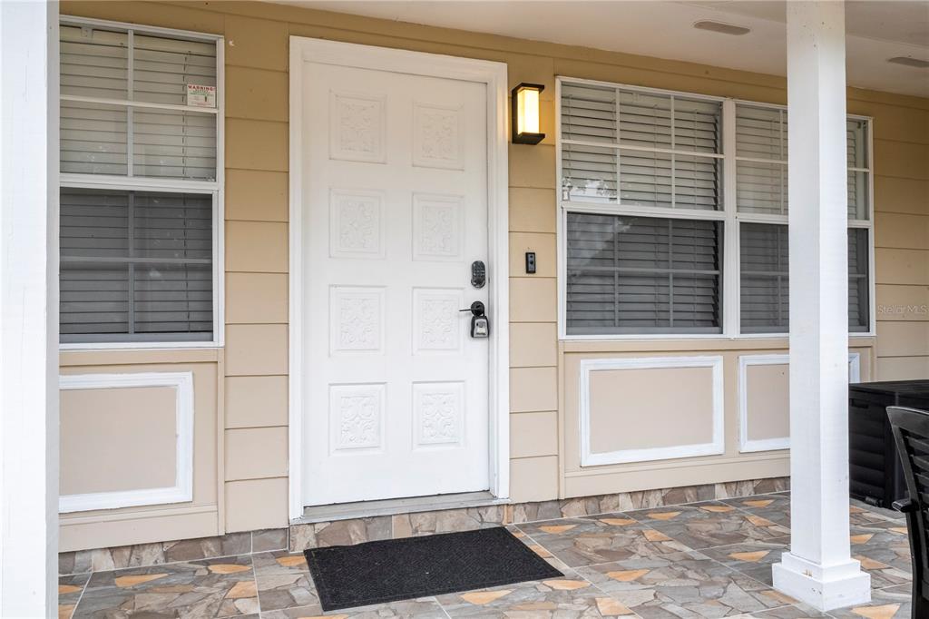 A white front door with a black mat sits on a tiled porch with siding — 1594 FRANCES STREET, KISSIMMEE, FL