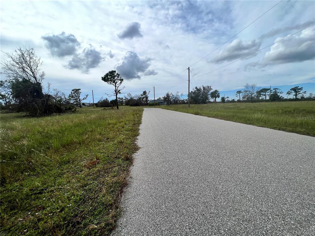 A paved road stretches through a grassy, open field under a cloudy sky — 27 DORISAN COURT, PLACIDA, FL
