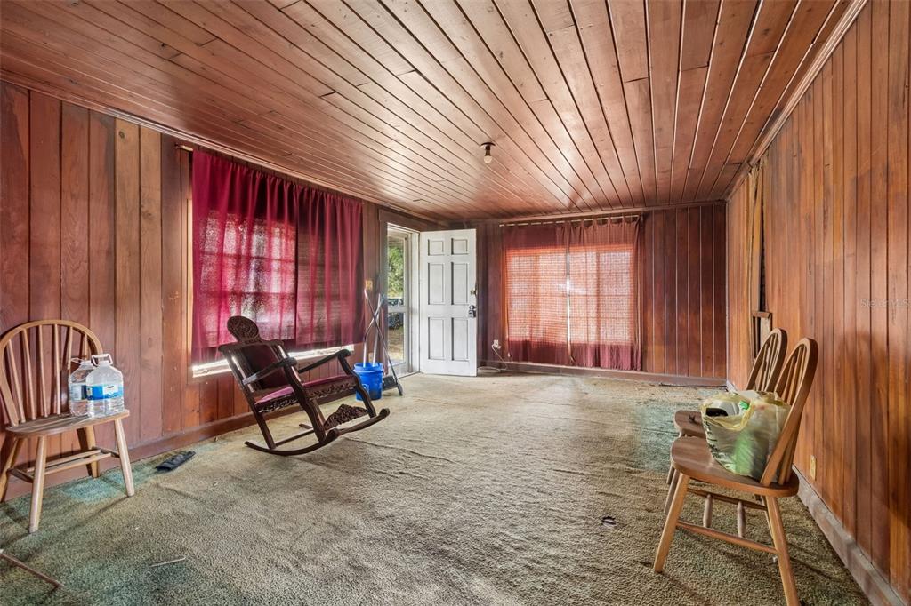A room with wood-paneled walls and ceiling, green carpet, a rocking chair, and two chairs — 2413 ED BROWN LANE, PLANT CITY, FL