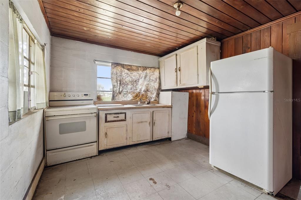 A kitchen features white appliances, wood-paneled ceilings, and painted concrete block walls — 2413 ED BROWN LANE, PLANT CITY, FL
