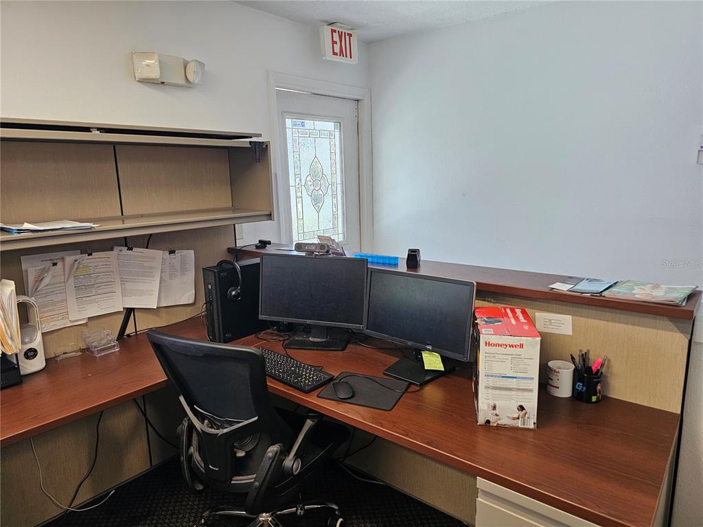 An office space features a wooden L-shaped desk, two computer monitors, and an exit door — 28960 US HIGHWAY 19 N UNIT 102, CLEARWATER, FL
