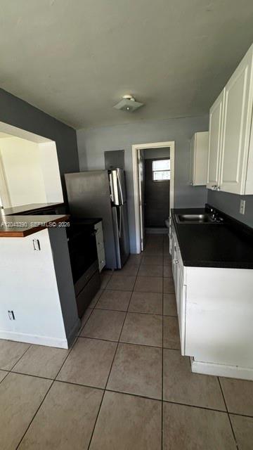 A kitchen features white cabinets, black countertops, stainless steel appliances, and light-colored tile flooring — FORT LAUDERDALE, FL