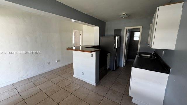 A kitchen with white cabinets, black countertops, and tile flooring opens to a living area — FORT LAUDERDALE, FL